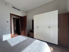 A bedroom with a bed, a wardrobe, a mirror, and a door leading to another room. - Furnished 2BR @AEON Towers, Sheikh Zayed (Giza Governorate)