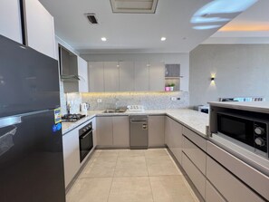 A modern kitchen with a black refrigerator, stainless steel appliances, and a marble countertop. - Furnished 2BR @AEON Towers, Sheikh Zayed (Giza Governorate)