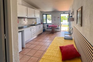 A compact kitchen with white cabinets, a dining area with a table and chairs, and a yellow bed with a red pillow. - A peaceful Fuseta escape with terrace, garden, and private parking. (Fuseta)