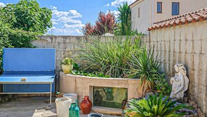 Eine Terrasse mit blauem Tisch, Blumentöpfen, einer Steinmauer und einer Statue.