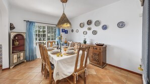 A dining area with a table set for four, surrounded by wooden chairs. A decorative hanging light fixture is above the table. - Relax with sunrise, sunset, and countryside scenery from your private terrace. (Estoi)