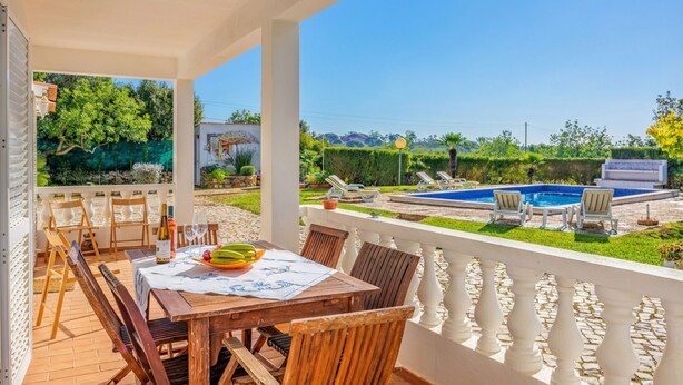 A covered outdoor dining area with a table set for two, a pool, and a view of the surrounding landscape. - Relax with sunrise, sunset, and countryside scenery from your private terrace. (Estoi)
