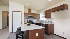 A modern kitchen with wooden cabinets, a central island, a microwave, and a dishwasher. - Serene 3-bedroom house perfect for relaxing stays in SeaTac, Burien, Seattle (SeaTac)