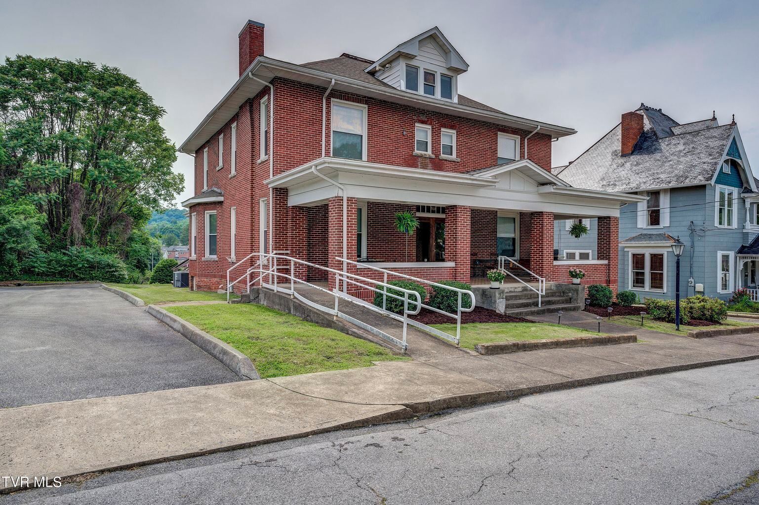 A two-story brick house with a front porch and a small front yard.