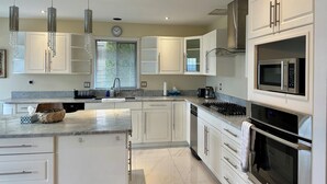 Una cucina moderna con mobili bianchi, un'isola centrale, elettrodomestici in acciaio inossidabile e lampade a sospensione.