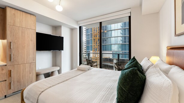 Una camera da letto moderna con un letto, una televisione, un armadio in legno e un balcone vista città.