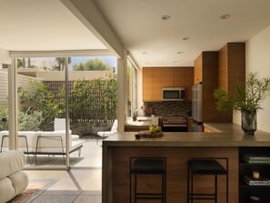 A modern kitchen with a large island, a dining area with a sofa and chairs, and a view of a garden. - Historic 1BR 2BR Retreat w Outdoor Shower & Private Patio in Palm Springs (Palm Springs)