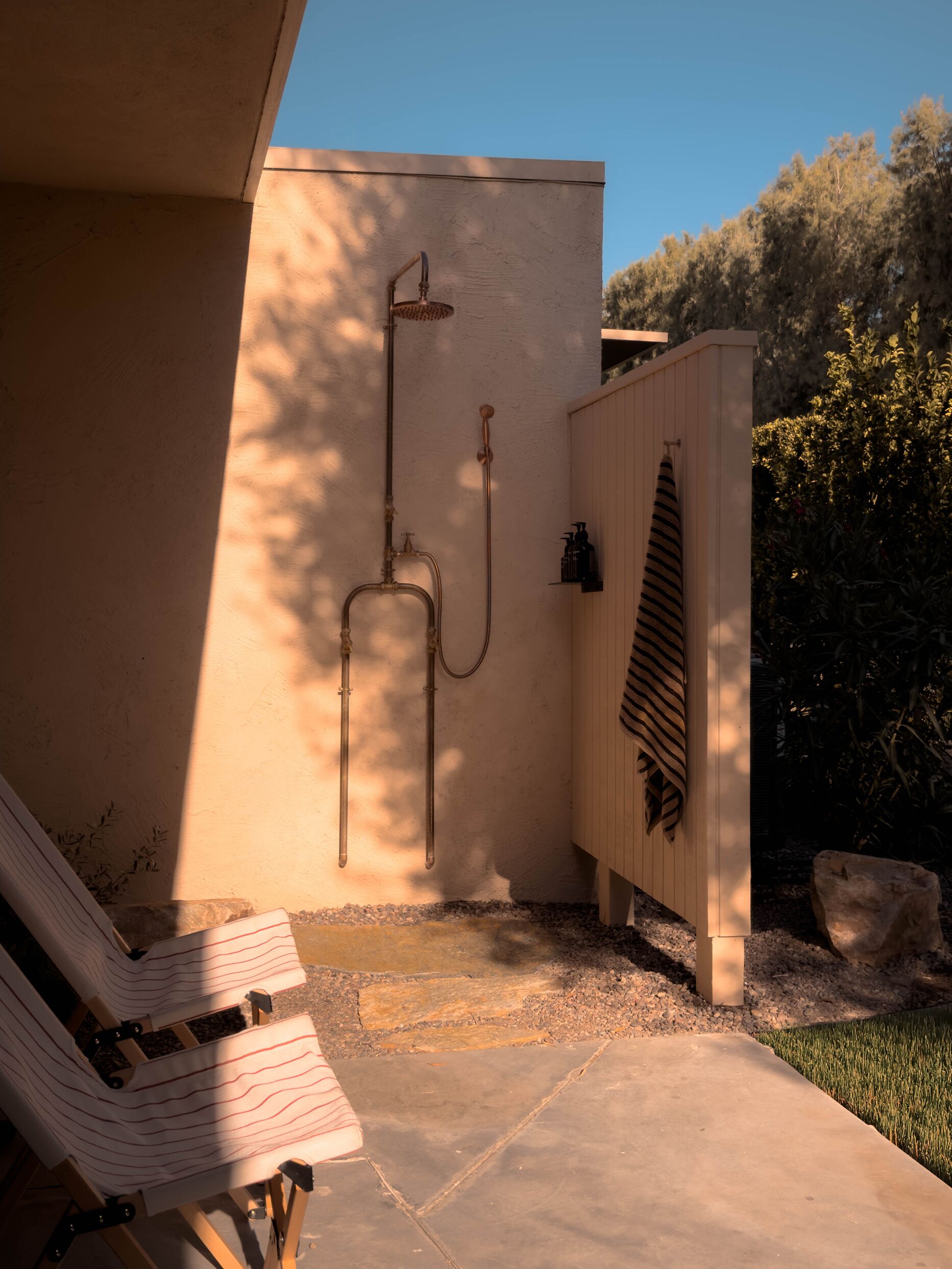 A spa area with a wooden bench, a wall-mounted shower, and a small garden with a rock and grass.