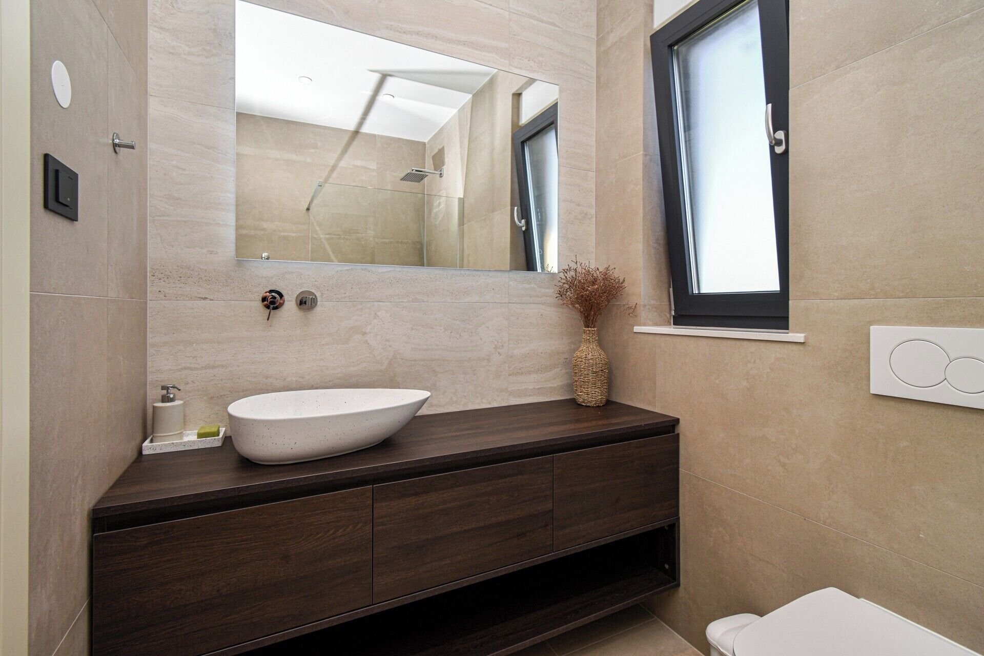 Un baño moderno con un espejo grande, un lavabo sobre encimera, armarios de madera oscura y un inodoro.