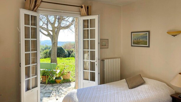 Une chambre à coucher comprenant un lit, une table de chevet, une fenêtre donnant sur un jardin et un radiateur.