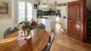 Un coin repas avec une table et des chaises en bois, un vase rempli de fleurs et, au fond, une cuisine.