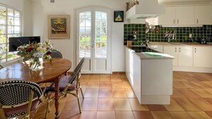 Une cuisine avec des meubles blancs, un plan de travail vert et un coin repas comprenant une table et des chaises en bois.
