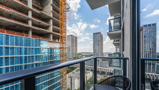 Uma varanda com vista para a paisagem urbana, incluindo edifícios altos e uma grua de construção.