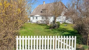 Ett vitt hus med ett sluttande tak, omgivet av ett vitt staket och en välskött gräsmatta.