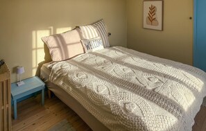 Un lit bien fait, recouvert d’une couverture blanche à texture intéressante, une table de chevet avec une lampe et une œuvre d’art encadrée accrochée au mur.