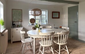 Un coin repas avec une table ronde et six chaises, une fenêtre avec vue, un luminaire suspendu et une porte.