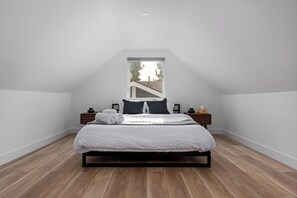 A bedroom with a sloped ceiling, a large window, a bed with white bedding, two bedside tables, and a wooden floor. - Spacious w/ 2BR 1Bath - Big Bear (Big Bear)