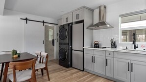 Une cuisine moderne avec un coin repas, comprenant un réfrigérateur à deux portes, un four encastré, une hotte en acier inoxydable et une fenêtre avec vue.