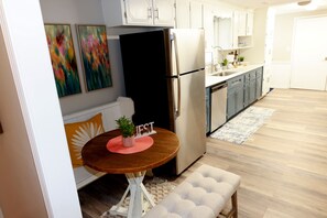 A modern kitchen with white cabinets, a black refrigerator, and a wooden dining table with a plant. - River's Edge Retreat in Muscle Shoals (Muscle Shoals)