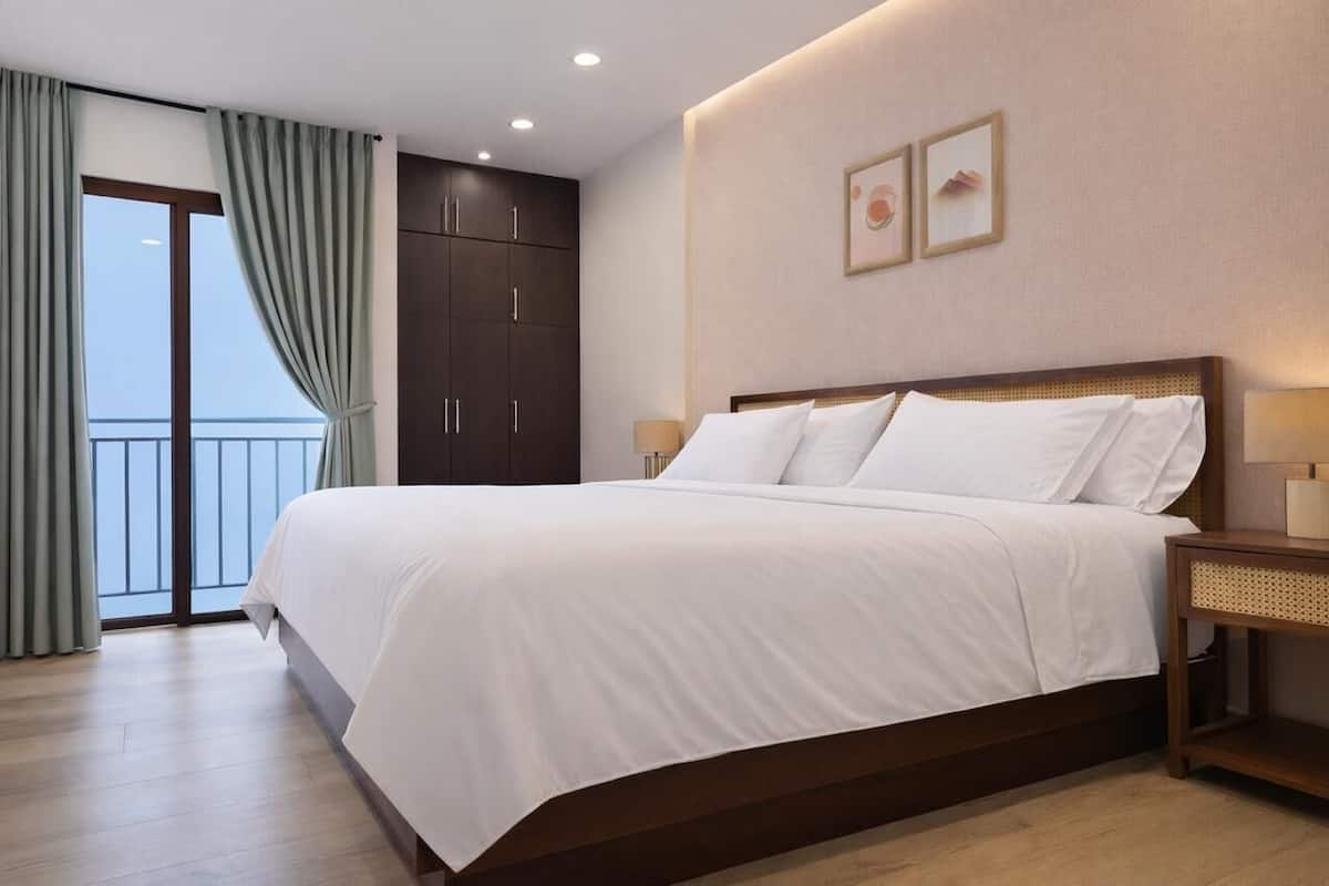 A hotel room with a large bed, a wardrobe, a bedside table, and a view of the outside.
