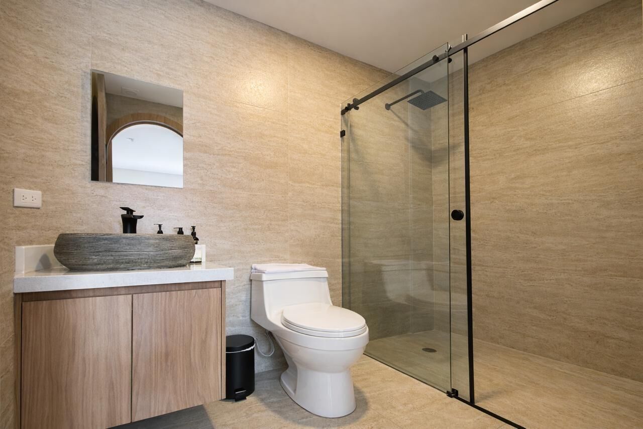 A modern bathroom with a large vessel sink, a toilet, and a glass-enclosed shower.