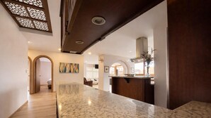 Una cocina moderna con encimeras de granito, techo de madera oscura y vistas al salón.