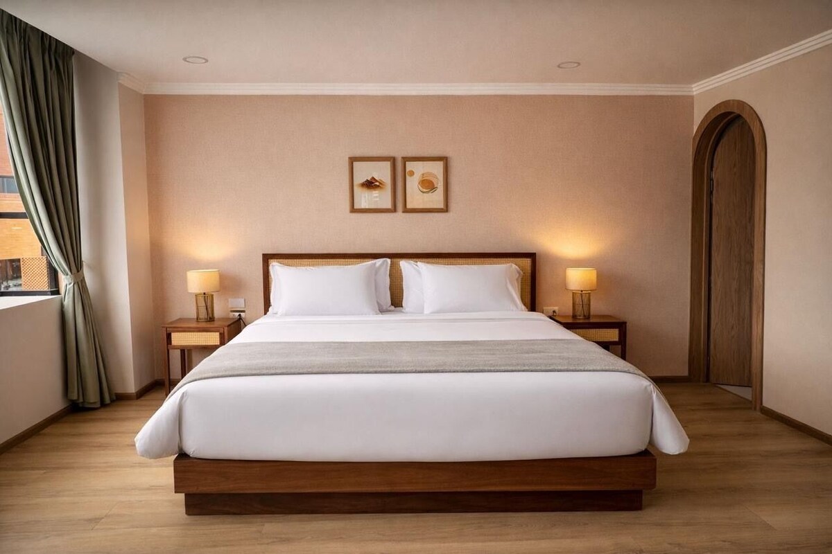 Una cama grande con sábanas blancas, dos mesitas de noche con lámparas, un cabecero de madera y un cuadro en la pared.