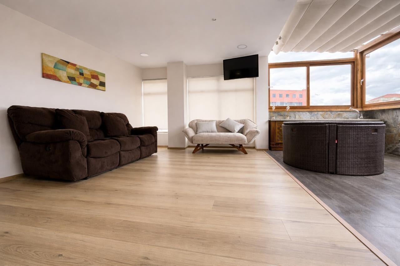 A spacious living area with a brown sofa, a light-colored armchair, and a wicker coffee table.
