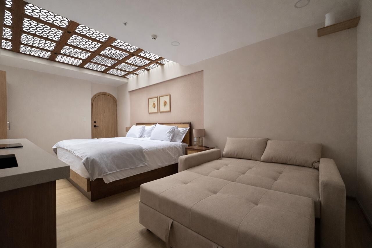 A modern bedroom with a bed, a sofa, a desk, and a ceiling with a geometric pattern.