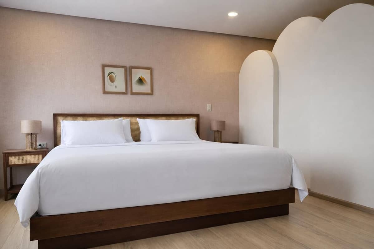 A hotel room with a large bed, two bedside tables with lamps, and two framed pictures on the wall.