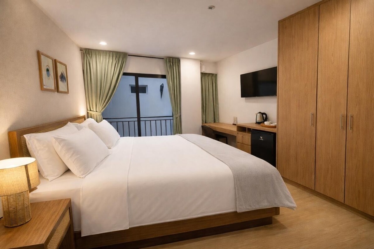 Una habitación de hotel con una cama grande, un escritorio con cafetera, un televisor montado en la pared y armarios de madera.