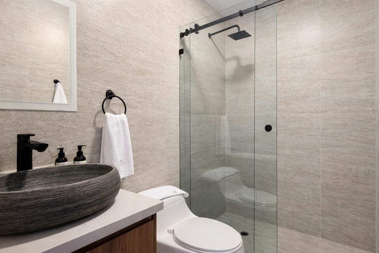 A modern bathroom with a large vessel sink, a toilet, and a glass-enclosed shower.