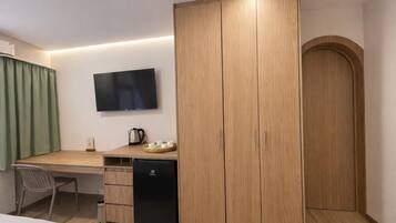 A hotel room with a wooden wardrobe, a desk with a television, a small refrigerator, and a green curtain.