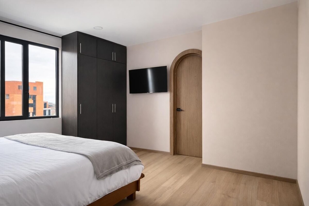 Un dormitorio con cama, armario oscuro, televisor y una puerta.