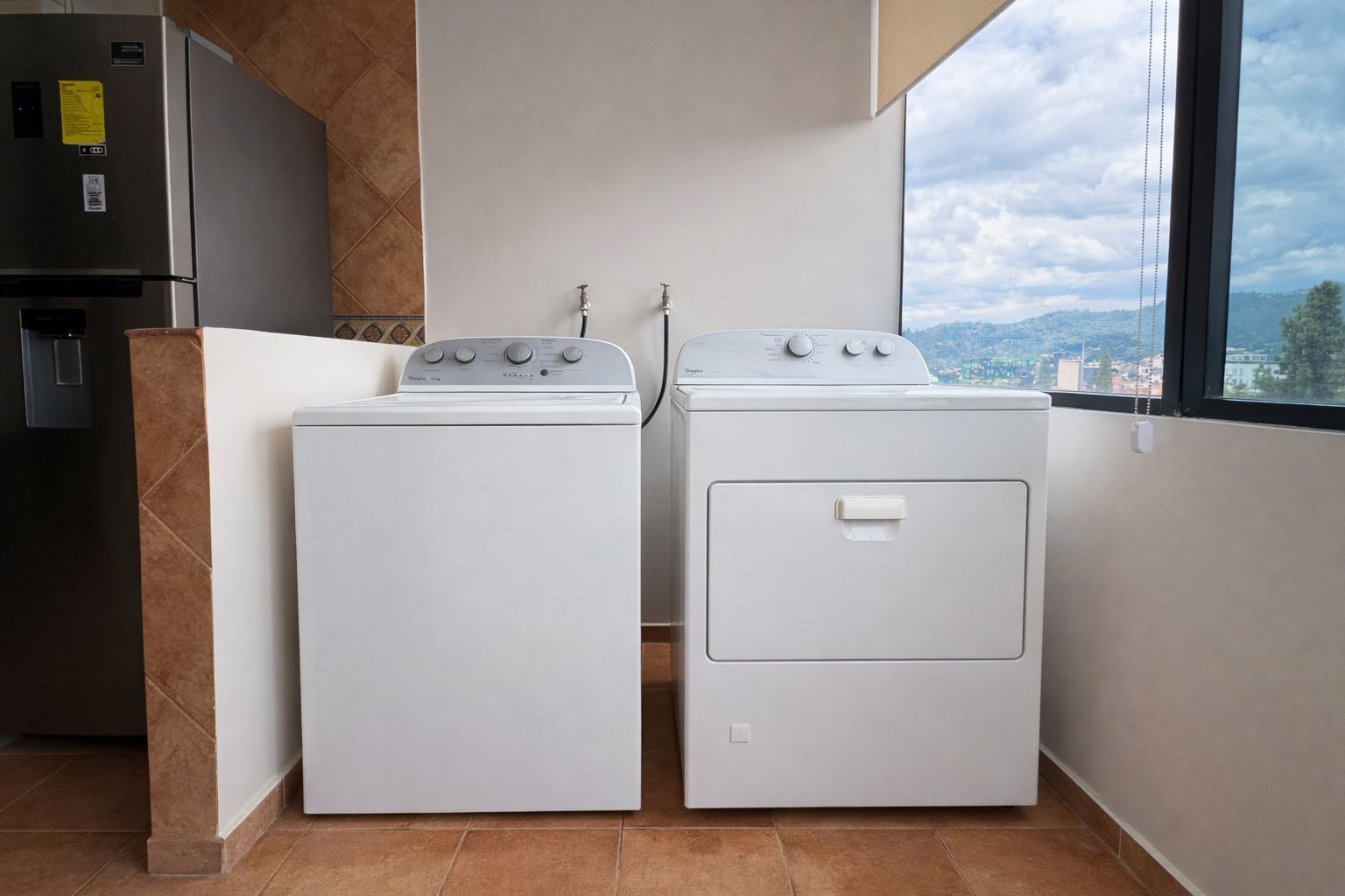 Een compacte keuken met een ingebouwde wasmachine en droger, een koelkast en een raam met uitzicht op de stad.