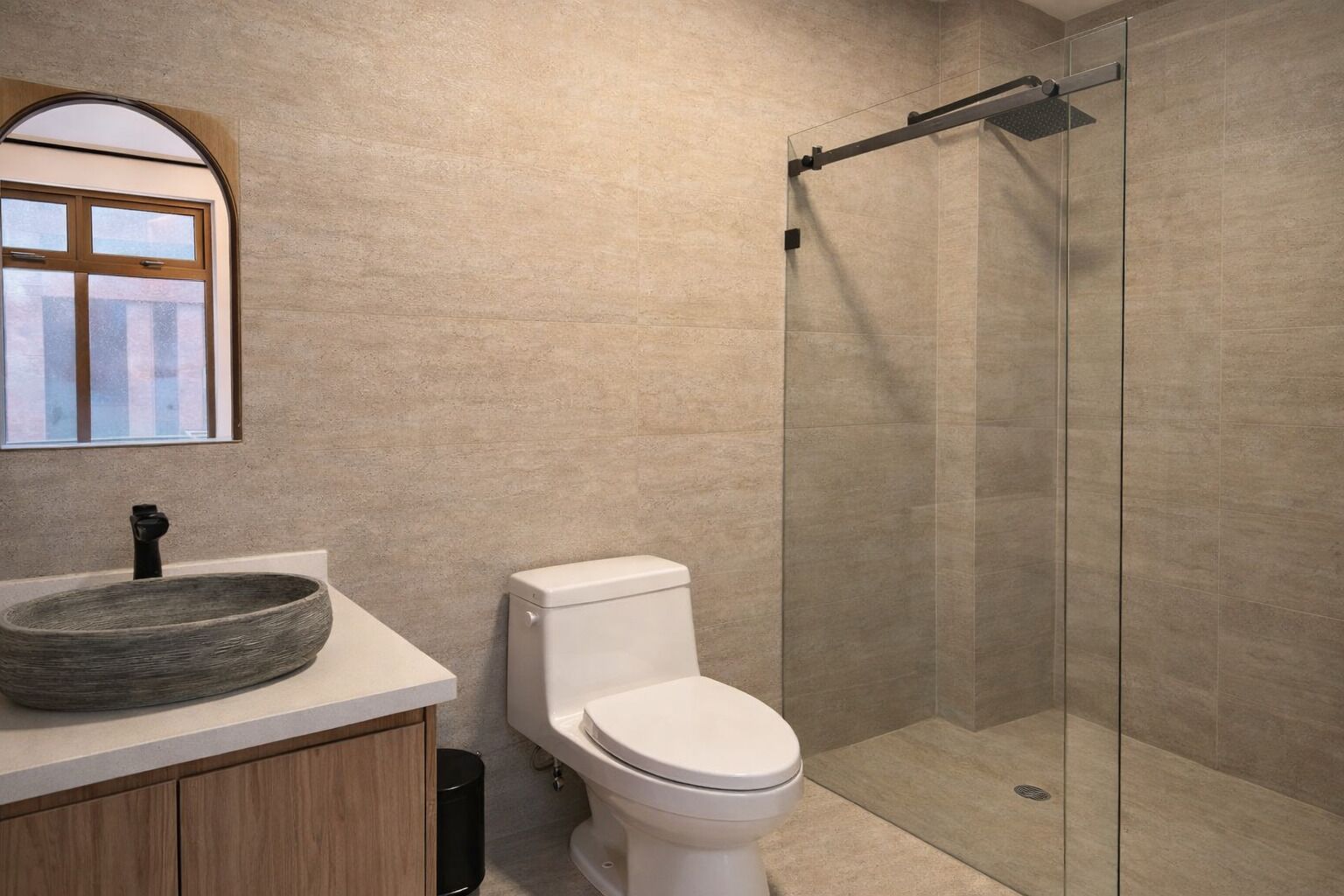 Une salle de bain moderne avec un lavabo rond, des toilettes et une douche à parois de verre.