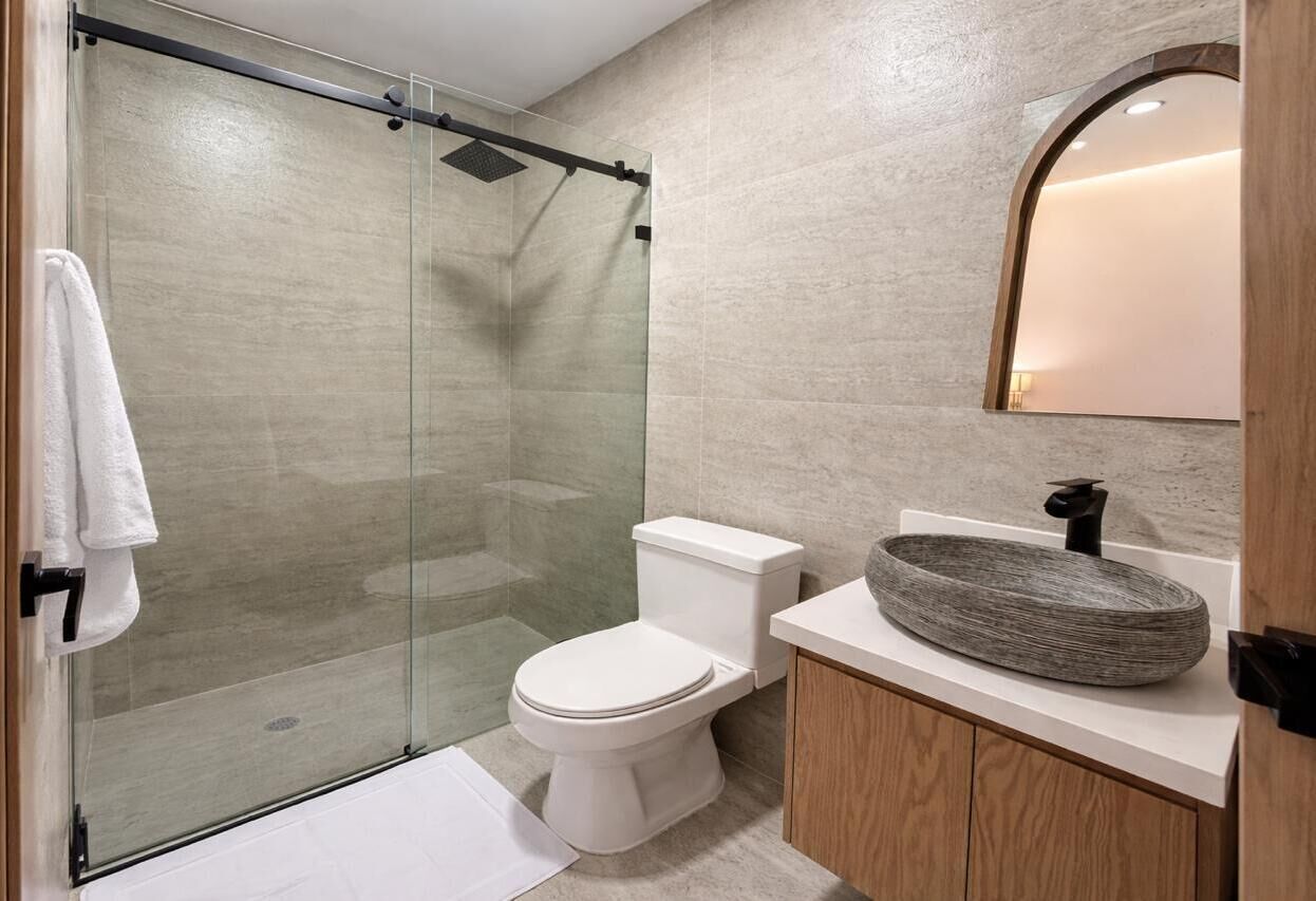 A modern bathroom with a glass-enclosed shower, a white toilet, and a wooden vanity with a large, round sink.