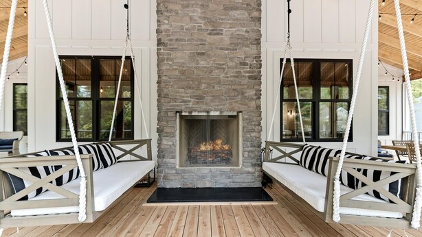 Une pièce chaleureuse avec une cheminée en pierre, un plancher en bois et deux fauteuils suspendus dotés de coussins à rayures.