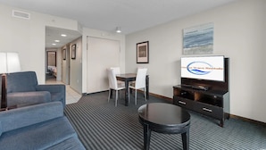 A hotel room with a TV displaying 'Ocean Wave Rentals,' a sofa, a dining table with chairs, and a small stool. - Experience the Ultimate Beachfront Lifestyle at Ocean's One (Myrtle Beach)