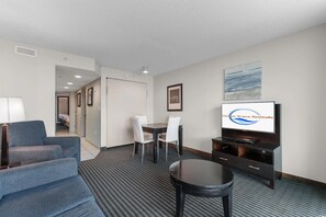 A hotel room with a TV displaying 'Ocean Wave Rentals,' a sofa, a dining table with chairs, and a small stool. - Experience the Ultimate Beachfront Lifestyle at Ocean's One (Myrtle Beach)