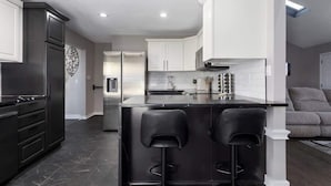 Una cocina moderna con armarios oscuros, una isla central con taburetes de bar y un salpicadero de azulejos blancos.