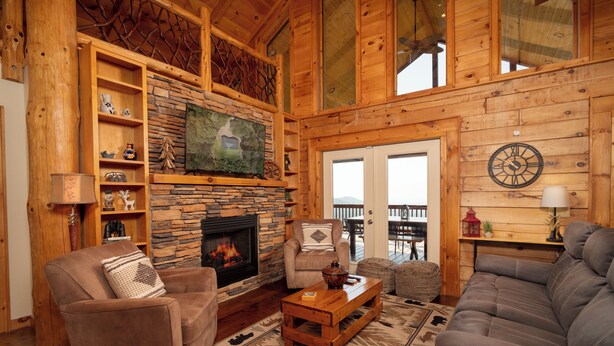 A cozy log cabin interior with a stone fireplace, wooden shelves, a comfortable seating area, and a balcony with a view. - Cozy 3BR/2.5BA Cabin Retreat on Buck Mountain, Purlear (Purlear)