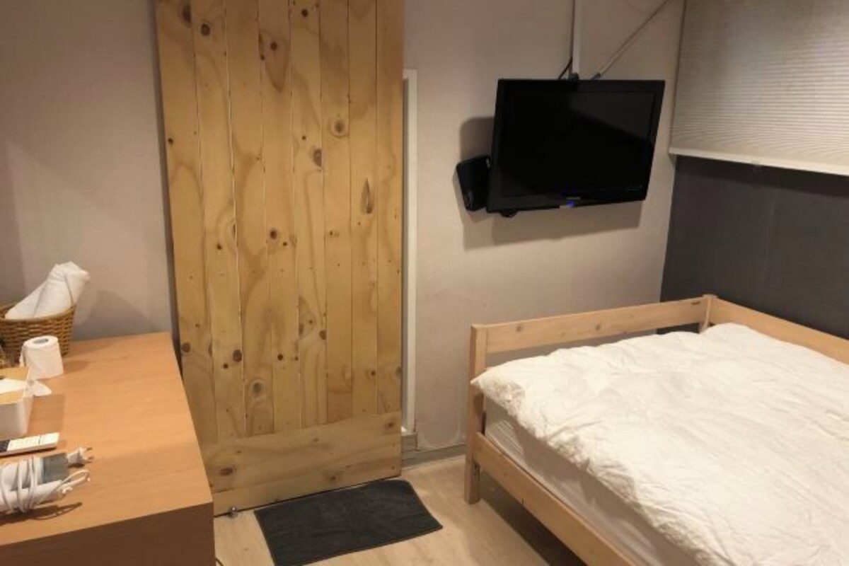 Een slaapkamer met een houten bed, een aan de muur bevestigde televisie en een houten garderobe.
