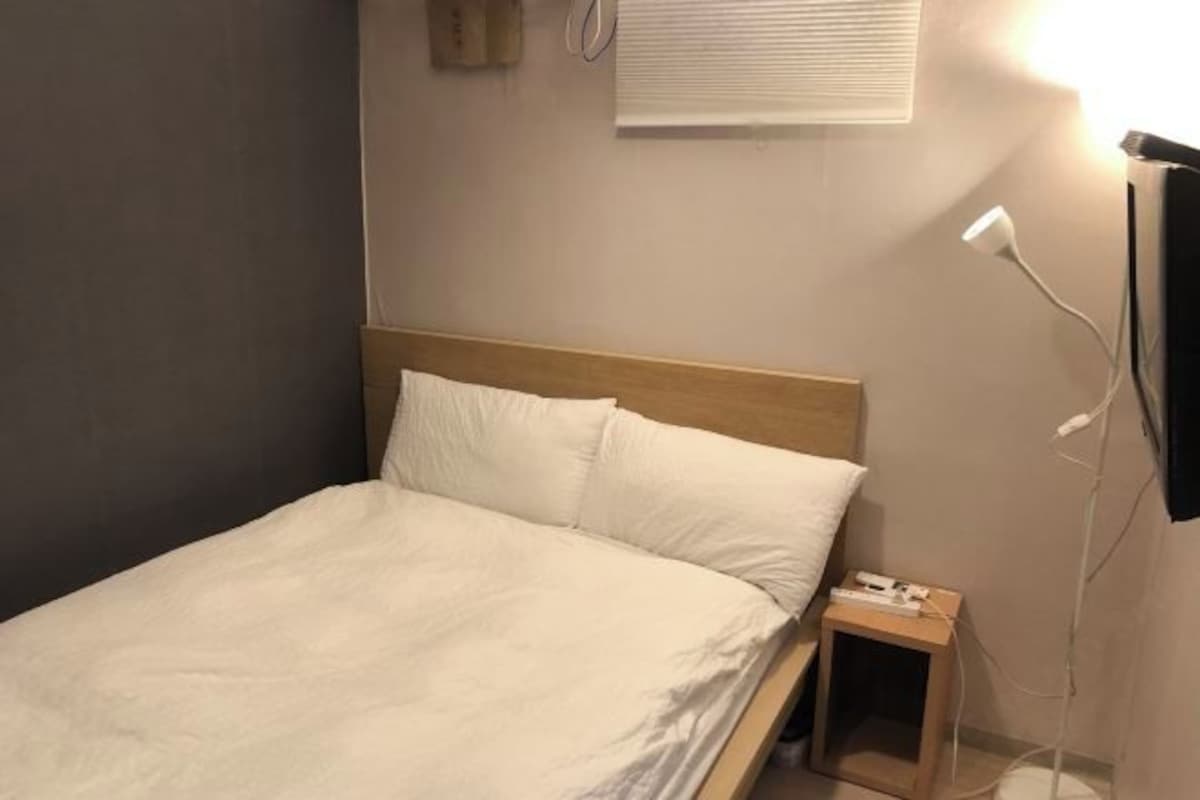 Een eenpersoonsbed met een houten hoofdbord, een nachtkastje met een lamp en een aan de muur bevestigde televisie.