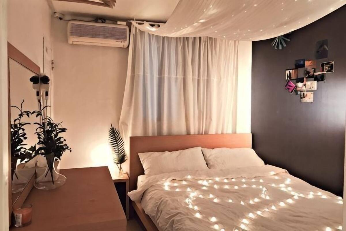 Quarto com cama, mesa de cabeceira com planta, ar-condicionado fixado na parede e parede com fotografias.
