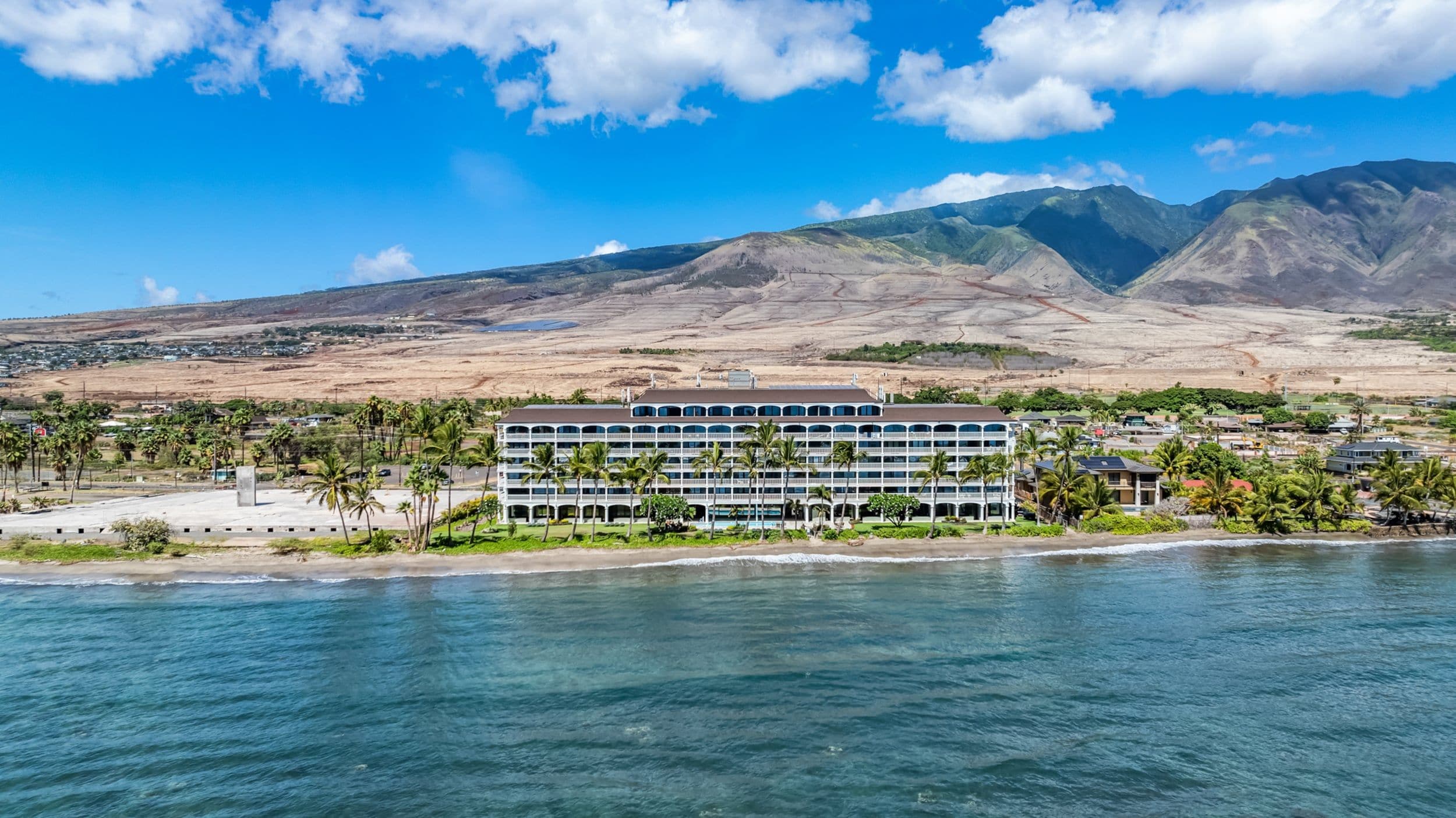 Un hôtel situé en bord de mer, doté de nombreux balcons, d’une piscine et offrant une vue sur l’océan et les montagnes.