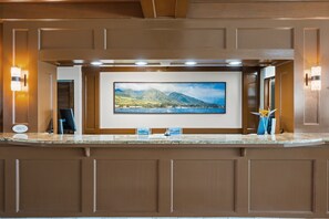 A reception area with a large framed picture of a mountainous landscape, a reception desk, and wall-mounted light fixtures. - Scenic West Maui Mountain View Escape (Lahaina)
