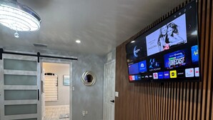 Una habitación de hotel moderna con un televisor de pantalla plana grande montado en la pared, una cama con edredón blanco y suelo de madera.
