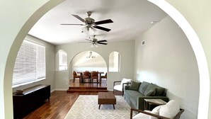 Un vaste espace de vie doté de planchers en bois franc, d’un ventilateur de plafond, d’un canapé vert, d’une table basse et d’un coin repas avec des chaises et une table.