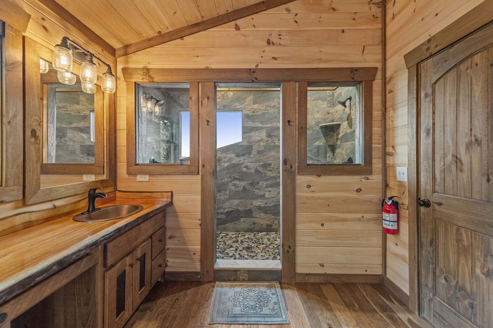 Interior de madera con un lavabo, espejo y pared de piedra.